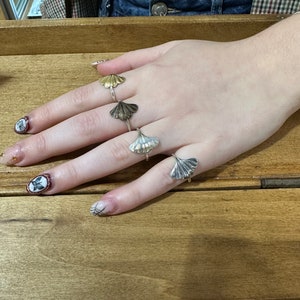 May include: Four silver and gold rings with a ginkgo leaf design. The rings are on a person's hand.