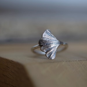 May include: A silver ring with a ginkgo leaf design. The leaf is detailed and textured, and the ring is simple and elegant.