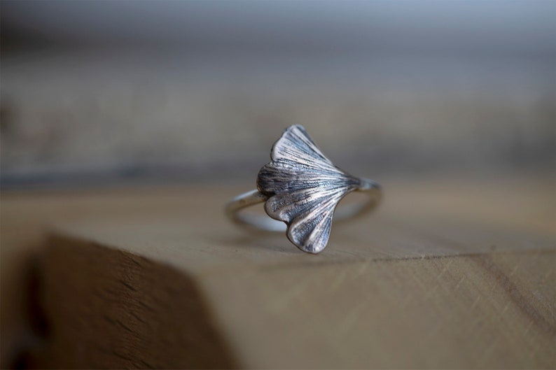May include: A silver ring with a ginkgo leaf design. The leaf is detailed and textured, and the ring is simple and elegant.