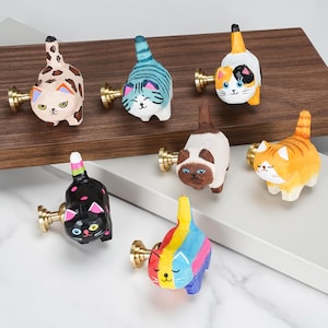 Puede incluir: Una colección de siete pomos de cajón de madera pintados a mano con forma de gato, cada uno con un patrón felino único que incluye atigrado, calicó, siamés y colores sólidos, unidos a soportes de latón pulido para muebles.