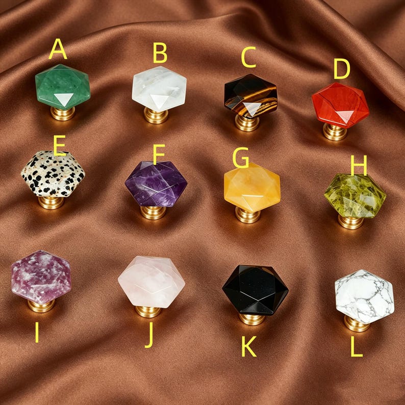 May include: A selection of twelve gemstone cabinet knobs in various colours and patterns. The knobs have a faceted, hexagonal shape and are mounted on brass hardware. Colours include green, white, black, red, purple, yellow, and speckled.