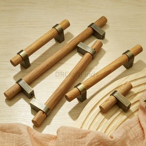 May include: A collection of five cabinet pulls featuring cylindrical light brown wooden handles paired with brushed brass metal mounting brackets. The hardware varies in length, with four long bar-style pulls and one smaller knob-style pull.