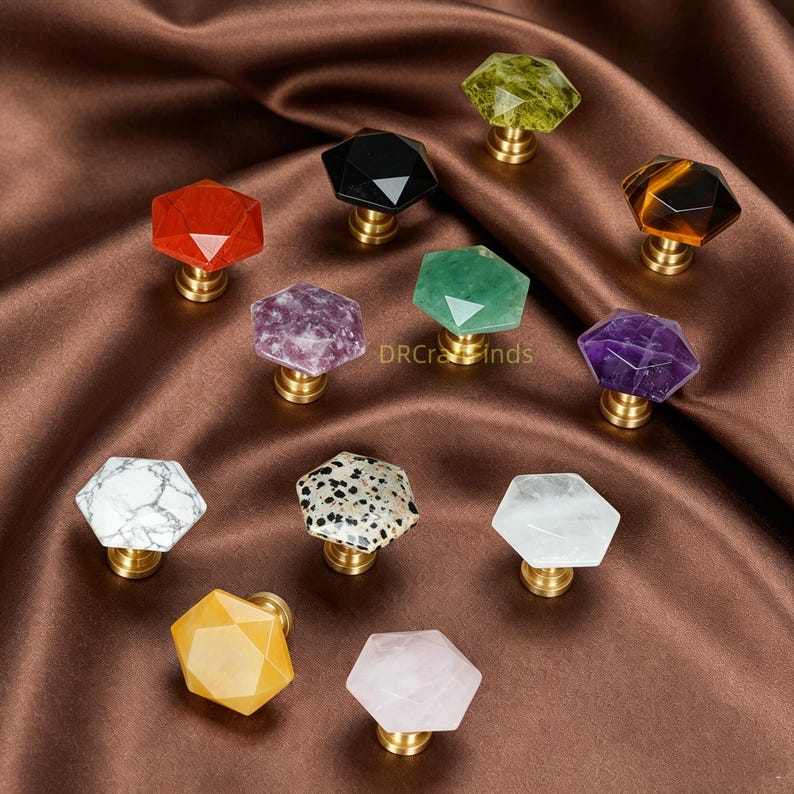 May include: A selection of gemstone cabinet knobs in diverse colours and patterns. Each knob has a faceted, hexagonal gemstone on a brass base. Colours include red, black, green, purple, white, yellow, and pink. The text "DRCraFinds" is visible.