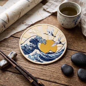May include: A circular embroidered patch featuring a large blue ocean wave, a bright yellow sun, and two white cranes in flight against a cream-colored background with radiating sunbeams. The design includes stylized clouds and a mountain peak.
