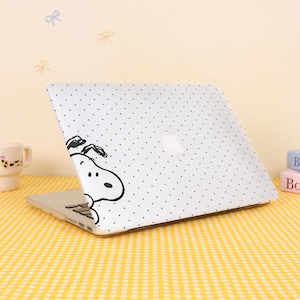 May include: A white laptop case with a black polka dot pattern and a black and white cartoon Snoopy graphic. The laptop is open on a yellow checkered surface.