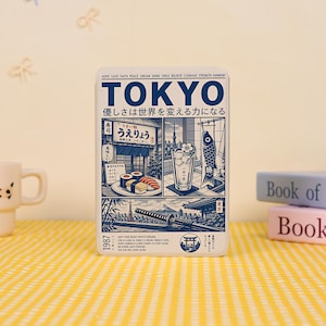 May include: A rectangular metal tin featuring a blue and white graphic design of Tokyo. The front displays the word TOKYO, Japanese text, illustrations of sushi, a glass of water, a koinobori, a katana, and Mount Fuji, with the year 1987.