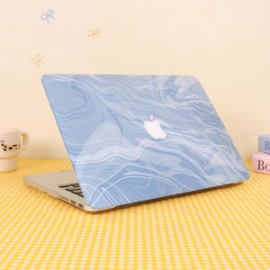 Könnte beinhalten: Ein hellblauer Laptop mit weißem Marmormuster. Der Laptop hat ein weißes Apple-Logo auf dem Cover. Der Laptop steht auf einer gelb-weiß karierten Oberfläche.