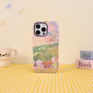 May include: A smartphone case featuring a colourful illustration of a sun with a face, rolling green hills, flying birds, and stylised flowers. The design incorporates a soft pink sky, orange and yellow floral elements, and a dark camera lens cutout.