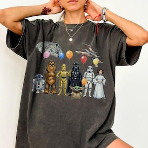 Peut inclure: T-shirt gris fonc&eacute; avec un motif Star Wars repr&eacute;sentant des personnages tels que R2-D2, Chewbacca, C-3PO, Dark Vador, un Stormtrooper et la Princesse Leia. Le motif comprend des ballons et des vaisseaux spatiaux. Le t-shirt est surdimensionn&eacute;.