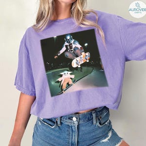 Puede incluir: Camiseta de color lila claro con un estampado gr&aacute;fico de The Mandalorian y Grogu patinando en un skate park. La imagen muestra a los personajes en el aire y en una patineta. La camiseta est&aacute; hecha de un material suave y tiene un corte holgado.