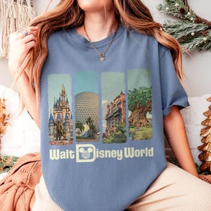Puede incluir: Una camiseta azul con cuatro paneles verticales que representan monumentos de Disney World. La camiseta muestra el texto "Walt Disney World" en blanco, acompa&ntilde;ado de un logotipo de Mickey Mouse. Las ilustraciones muestran un castillo, una esfera, un edificio y un &aacute;rbol.