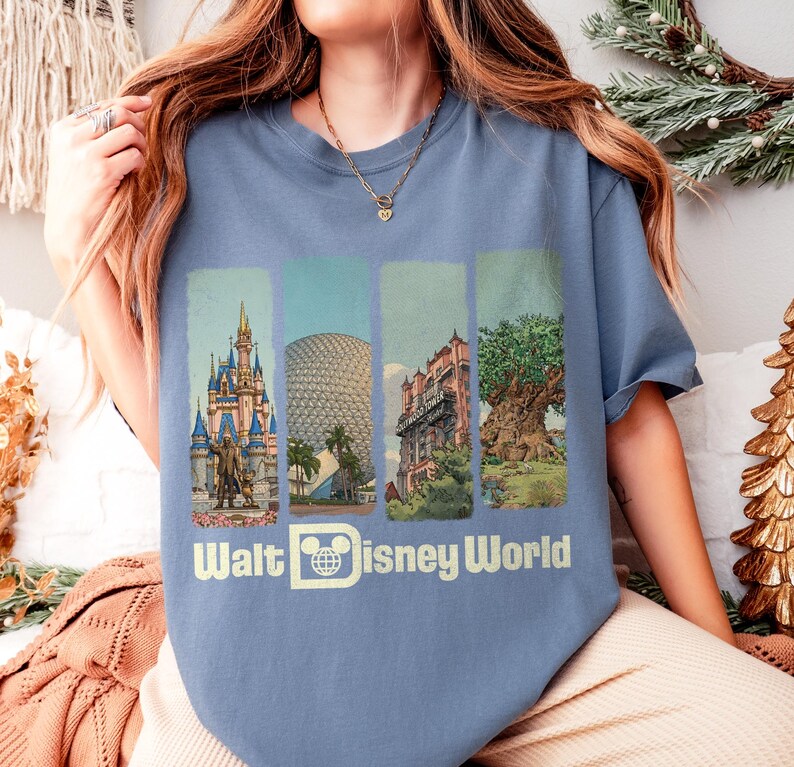 Puede incluir: Una camiseta azul con cuatro paneles verticales que representan monumentos de Disney World. La camiseta muestra el texto "Walt Disney World" en blanco, acompa&ntilde;ado de un logotipo de Mickey Mouse. Las ilustraciones muestran un castillo, una esfera, un edificio y un &aacute;rbol.
