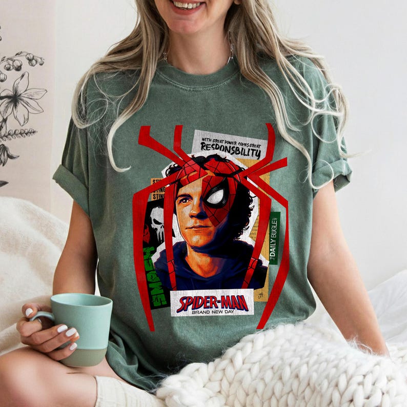 Op de afbeelding: Groen t-shirt met een Spider-Man-afbeelding. Het ontwerp bevat een portret van Spider-Man, een rood spinnenweb en de tekst "SPIDER-MAN BRAND NEW DAY" en "WITH GREAT POWER COMES GREAT RESPONSIBILITY".