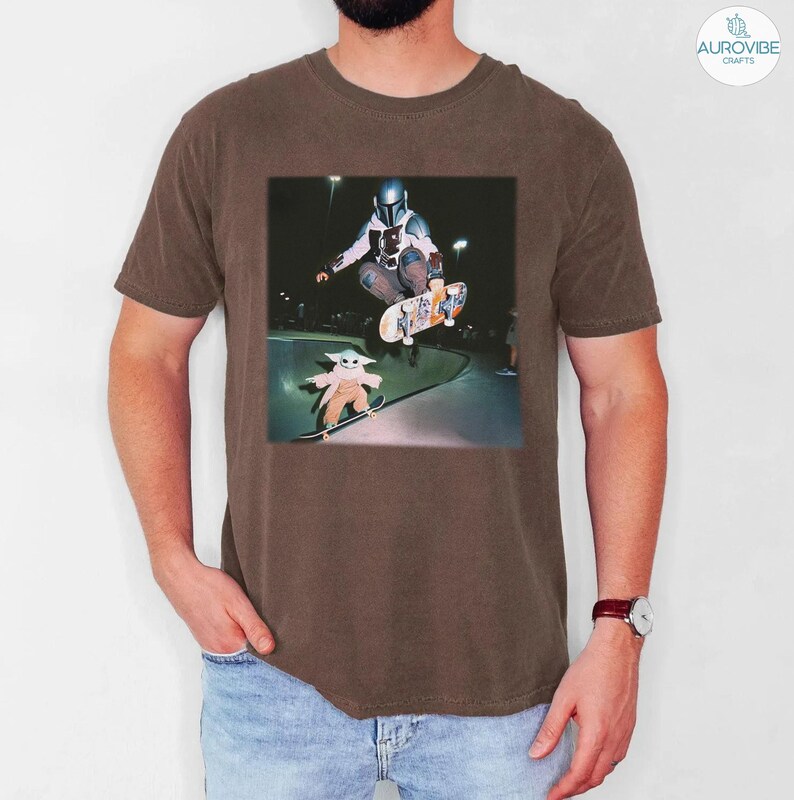Puede incluir: Camiseta marr&oacute;n con un gr&aacute;fico de un skater y un personaje de una popular serie de ciencia ficci&oacute;n. El gr&aacute;fico muestra al skater en el aire, realizando un truco, con otro personaje patinando debajo.