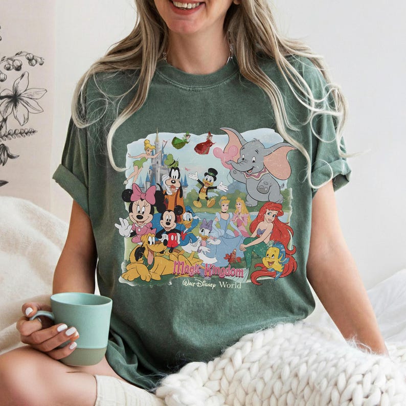 Puede incluir: Camiseta verde con un gr&aacute;fico colorido de personajes de Disney, incluyendo Mickey Mouse, Minnie Mouse, Donald Duck y Ariel. El gr&aacute;fico incluye el texto "Magic Kingdom, Walt Disney World".