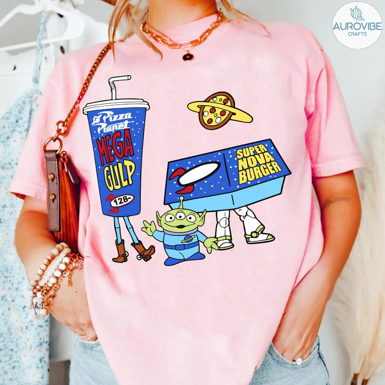 以下が含まれることがあります： ピンク色のTシャツ。メガガルのプドリンク、ピザ、スーパーノヴァバーガー、緑色のエイリアンの漫画グラフィックが特徴です。メガガルのプには128の数字があります。シャツには飲み物に「Pizza Planet」の文字が入っています。