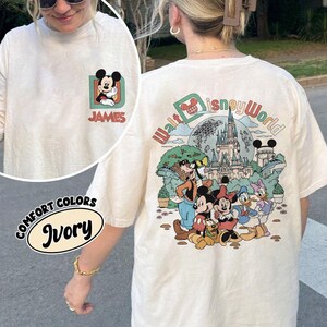 May include: Ivory-colored long-sleeve t-shirt featuring a Mickey Mouse graphic on the front with the name "JAMES" and a larger "Walt Disney World" graphic on the back. The shirt has a crew neck and is made of a soft material.