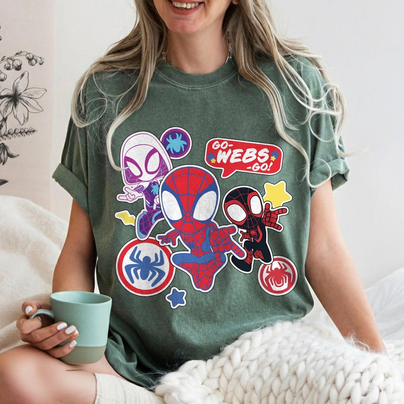 Puede incluir: Camiseta verde con un dise&ntilde;o de dibujos animados de tres personajes de Spider-Man. El dise&ntilde;o incluye a Spider-Man, Spider-Gwen y un Spider-Man negro, junto con el texto "GO WEBS - GO!". La camiseta tiene cuello redondo y mangas cortas.