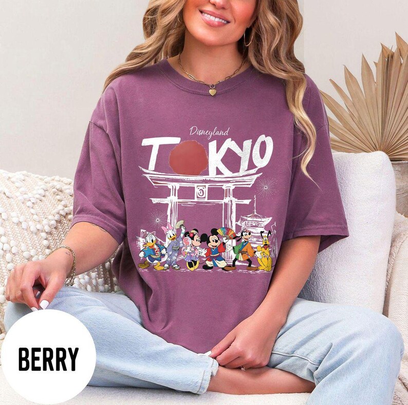Puede incluir: Camiseta color bayas con un gr&aacute;fico de Disneyland Tokyo. El dise&ntilde;o incluye la palabra "TOKYO" en blanco, un sol rojo y varios personajes de Disney. La camiseta tiene mangas cortas.