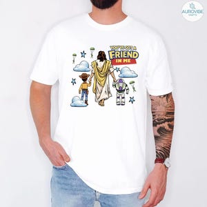 May include: White t-shirt featuring a graphic with the text "YOU'VE GOT A FRIEND IN ME". The graphic depicts a figure in a white robe, holding hands with a cartoon cowboy and a space ranger. Blue clouds, stars, and parachutes are also included in the design.