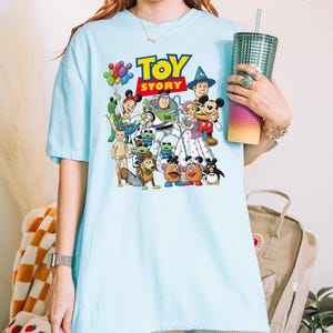 Op de afbeelding: Lichtblauw T-shirt met een kleurrijke afbeelding van personages uit de animatiefilm "Toy Story". Het ontwerp bevat het logo van de film en verschillende personages zoals Woody, Buzz Lightyear en Mr. Potato Head. Het shirt heeft korte mouwen en een losse pasvorm.