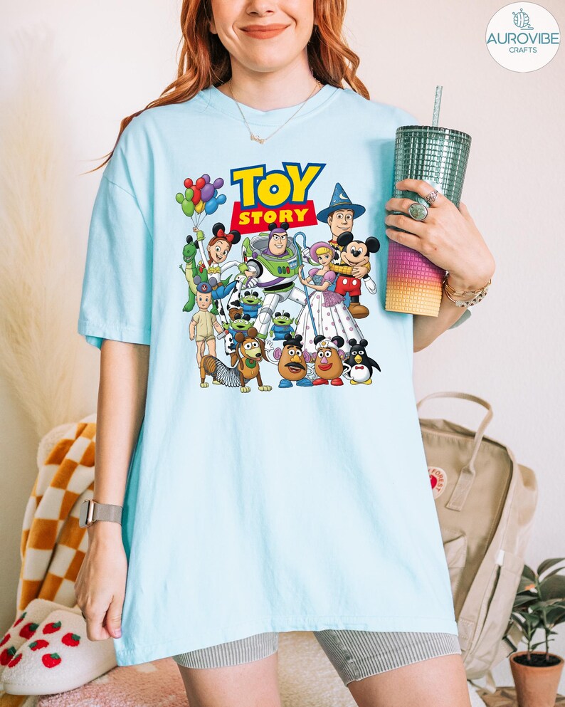 Op de afbeelding: Lichtblauw T-shirt met een kleurrijke afbeelding van personages uit de animatiefilm "Toy Story". Het ontwerp bevat het logo van de film en verschillende personages zoals Woody, Buzz Lightyear en Mr. Potato Head. Het shirt heeft korte mouwen en een losse pasvorm.