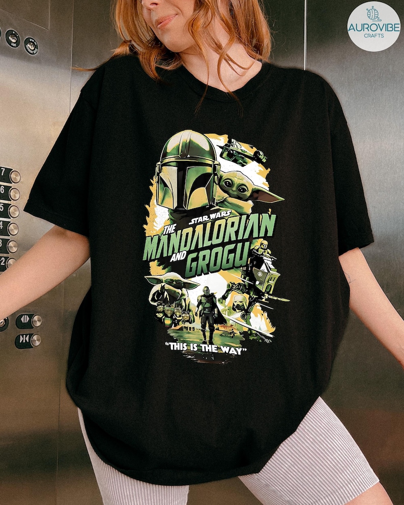 Pode incluir: Camiseta preta com um gr&aacute;fico de Star Wars com "The Mandalorian and Grogu". O design inclui o capacete do Mandaloriano, Grogu e a frase "This is the Way".