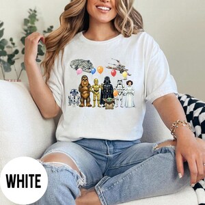 Peut inclure: T-shirt blanc avec un motif color&eacute; de personnages de Star Wars, dont R2-D2, Chewbacca, C-3PO, Dark Vador, un Stormtrooper, la Princesse Leia et Baby Yoda. Le motif comprend des ballons et des vaisseaux spatiaux.