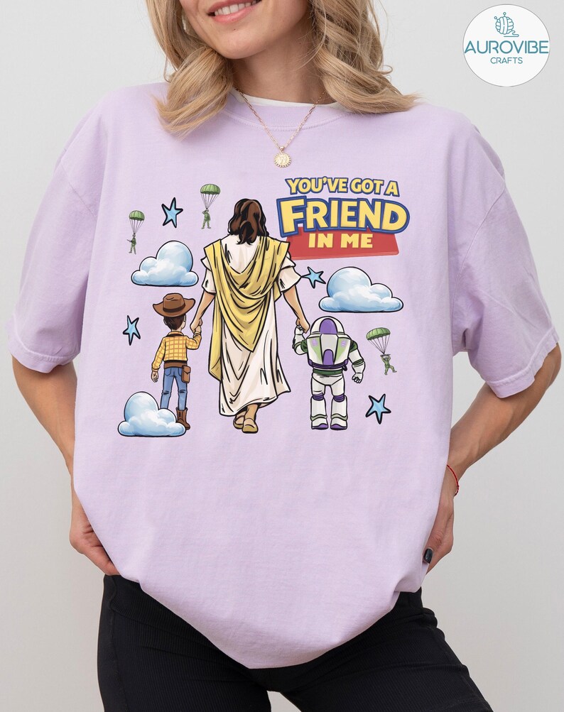 May include: Light purple t-shirt with the text "YOU'VE GOT A FRIEND IN ME". The graphic features cartoon illustrations of Jesus, a cowboy, and a space ranger, with clouds, stars, and parachutes.