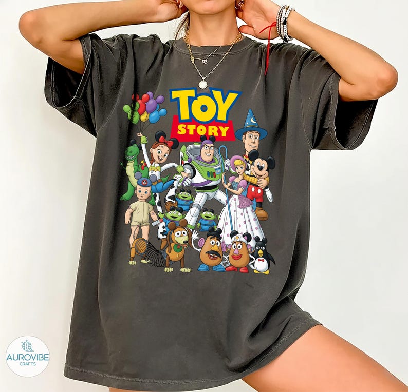 Op de afbeelding: Donkergrijs T-shirt met het "Toy Story" logo in geel en blauw. Het shirt toont een kleurrijke afbeelding van verschillende personages uit de animatiefilm, waaronder Buzz Lightyear, Woody en Mickey Mouse.