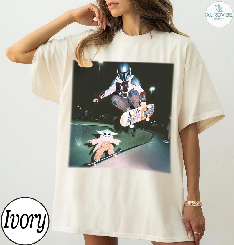 Puede incluir: Camiseta color marfil con un gr&aacute;fico de un skater y Grogu patinando en un skate park. El skater lleva casco y armadura. Grogu lleva un abrigo color beige. La camiseta tiene un corte holgado y la palabra "Ivory" est&aacute; impresa en la parte inferior.