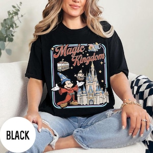 May include: Black t-shirt with a colorful graphic featuring Mickey Mouse in a sorcerer's outfit, the words "Magic Kingdom", and a castle. The shirt is a classic crew neck style.