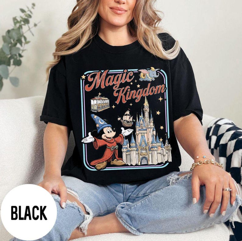 May include: Black t-shirt with a colorful graphic featuring Mickey Mouse in a sorcerer's outfit, the words "Magic Kingdom", and a castle. The shirt is a classic crew neck style.