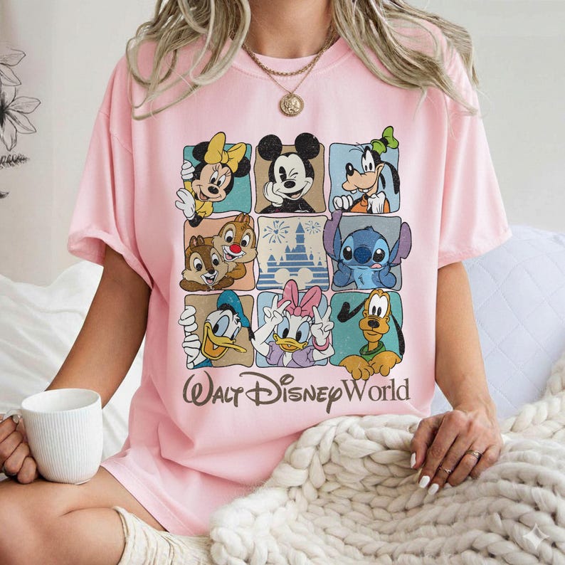 May include: A light pink t-shirt featuring a grid of Disney characters including Mickey Mouse, Minnie Mouse, Goofy, Donald Duck, and Stitch. The words "Walt Disney World" are printed in a brown script font below the grid.