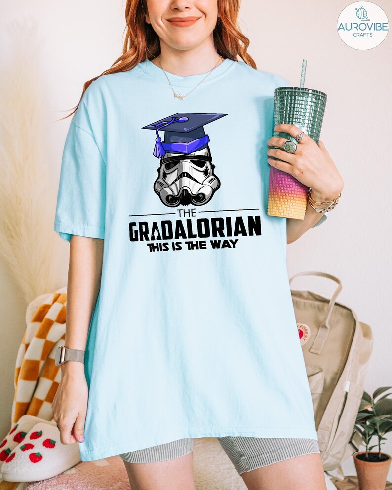 Pu&ograve; includere: T-shirt azzurra con un casco da Stormtrooper con cappello di laurea. Il testo "THE GRADALORIAN THIS IS THE WAY" &egrave; stampato sotto. La maglietta &egrave; in stile casual.