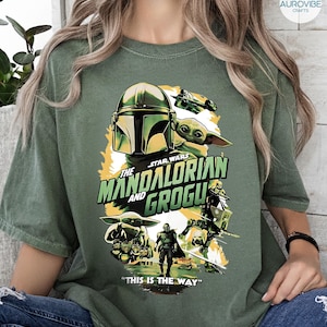Pode incluir: Camiseta verde com um gr&aacute;fico de "The Mandalorian" com o texto "The Mandalorian and Grogu" e "This is the Way". O design inclui imagens de The Mandalorian, Grogu e outros personagens da s&eacute;rie Star Wars.