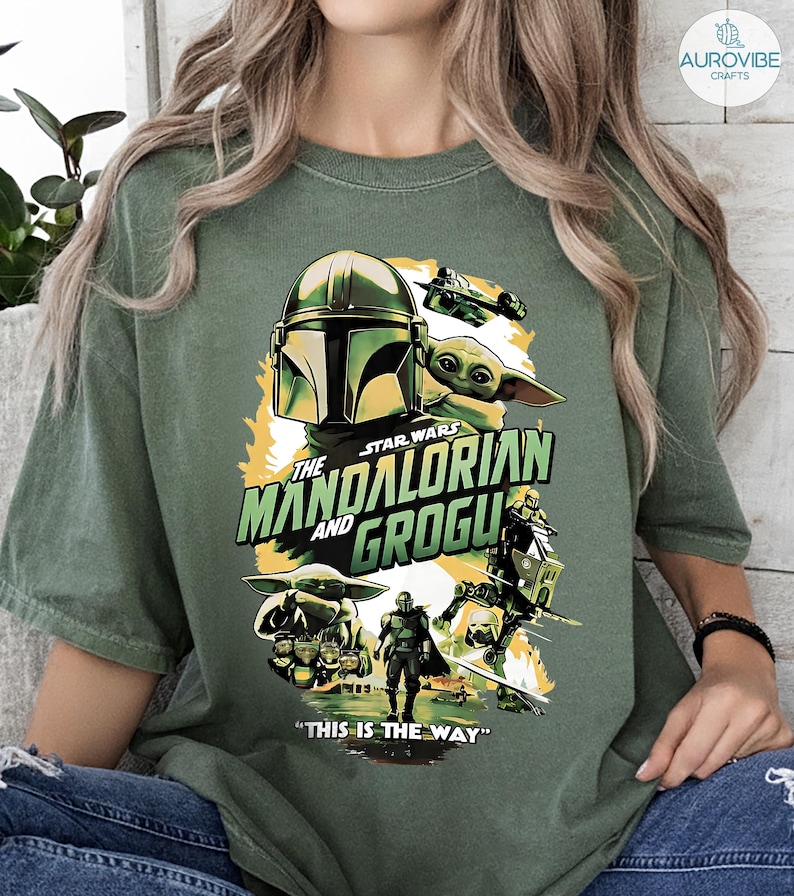 Pode incluir: Camiseta verde com um gr&aacute;fico de "The Mandalorian" com o texto "The Mandalorian and Grogu" e "This is the Way". O design inclui imagens de The Mandalorian, Grogu e outros personagens da s&eacute;rie Star Wars.