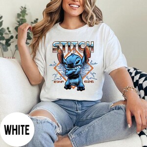 Puede incluir: Camiseta blanca con un dise&ntilde;o de personaje de dibujos animados azul, con la palabra "STITCH" en un estilo retro. El personaje est&aacute; sobre un dise&ntilde;o de rayo en forma de diamante, con "626" y "GKP" debajo.