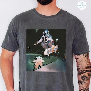 Puede incluir: Camiseta gris oscuro con un gr&aacute;fico de un skater con armadura haciendo un truco, y un personaje m&aacute;s peque&ntilde;o patinando debajo. La imagen est&aacute; ambientada en un parque de skate por la noche.
