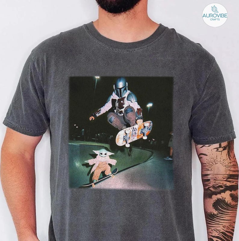 Puede incluir: Camiseta gris oscuro con un gr&aacute;fico de un skater con armadura haciendo un truco, y un personaje m&aacute;s peque&ntilde;o patinando debajo. La imagen est&aacute; ambientada en un parque de skate por la noche.
