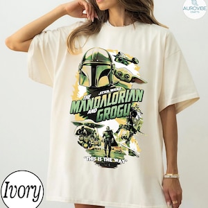 Pode incluir: Camiseta cor marfim com um design gr&aacute;fico de "The Mandalorian and Grogu". O design inclui o capacete do Mandaloriano, Grogu e a frase "This is the Way". A camiseta tem um corte folgado.