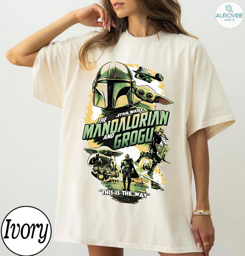 Pode incluir: Camiseta cor marfim com um design gr&aacute;fico de "The Mandalorian and Grogu". O design inclui o capacete do Mandaloriano, Grogu e a frase "This is the Way". A camiseta tem um corte folgado.