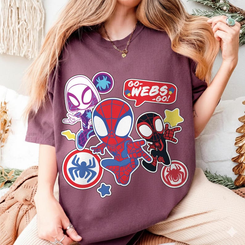 Puede incluir: Camiseta granate con ilustraciones de dibujos animados de personajes de Spider-Man. El dise&ntilde;o incluye a Spider-Man, Spider-Gwen y Miles Morales, con bocadillos que dicen "GO-WEBS-GO!" y emblemas de ara&ntilde;a.