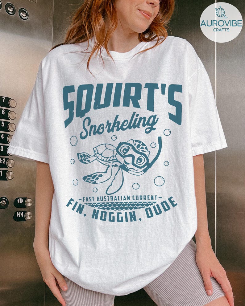May include: White t-shirt with a teal graphic featuring a cartoon turtle wearing a snorkel mask. The text reads "Squirt's Snorkeling" above the turtle and "Fin, Noggin, Dude" below, with "-East Australian Current-" in between.