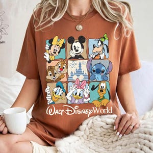 May include: A brown t-shirt featuring a grid of Disney characters including Mickey Mouse, Minnie Mouse, Goofy, Chip and Dale, Stitch, Donald Duck, Daisy Duck, and Pluto. The words "Walt Disney World" are printed below the grid in white.