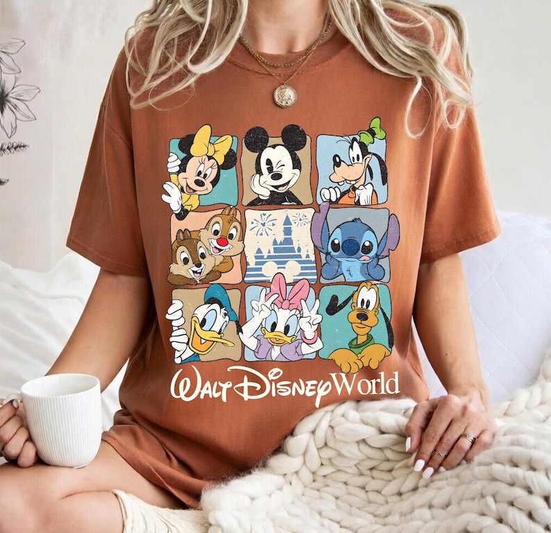 May include: A brown t-shirt featuring a grid of Disney characters including Mickey Mouse, Minnie Mouse, Goofy, Chip and Dale, Stitch, Donald Duck, Daisy Duck, and Pluto. The words "Walt Disney World" are printed below the grid in white.