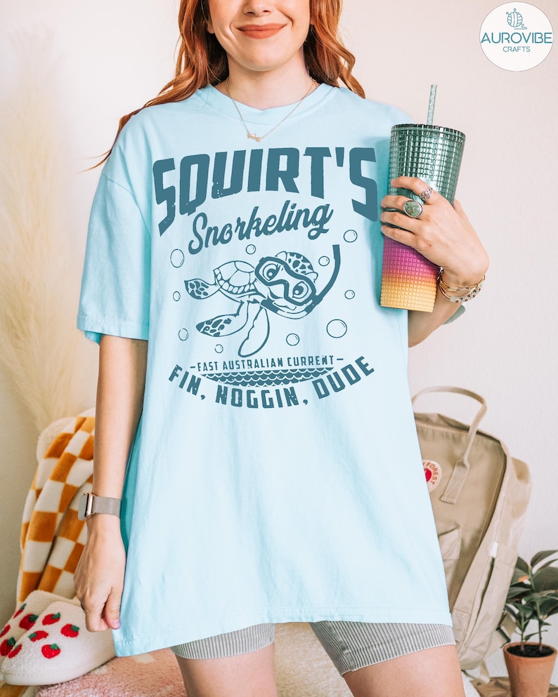 May include: Light blue t-shirt with the text "Squirt's Snorkeling" and a cartoon turtle wearing goggles. The shirt also features the phrase "East Australian Current - Fin, Noggin, Dude."