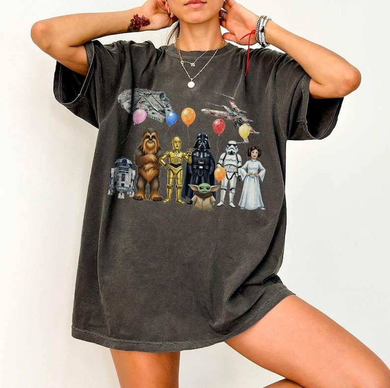 Peut inclure: T-shirt gris fonc&eacute; avec un motif Star Wars repr&eacute;sentant des personnages tels que R2-D2, Chewbacca, C-3PO, Dark Vador, un Stormtrooper et la Princesse Leia. Le motif comprend des ballons et des vaisseaux spatiaux. Le t-shirt est surdimensionn&eacute;.