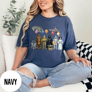 Peut inclure: T-shirt bleu marine avec un motif Star Wars repr&eacute;sentant divers personnages, vaisseaux spatiaux et ballons. Le design comprend R2-D2, Chewbacca, C-3PO, Dark Vador, un Stormtrooper, la Princesse Leia et Baby Yoda. Le mot "NAVY" est imprim&eacute; sur un cercle blanc.