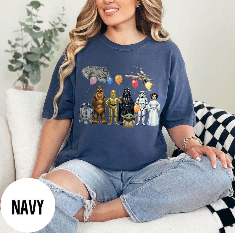 Peut inclure: T-shirt bleu marine avec un motif Star Wars repr&eacute;sentant divers personnages, vaisseaux spatiaux et ballons. Le design comprend R2-D2, Chewbacca, C-3PO, Dark Vador, un Stormtrooper, la Princesse Leia et Baby Yoda. Le mot "NAVY" est imprim&eacute; sur un cercle blanc.